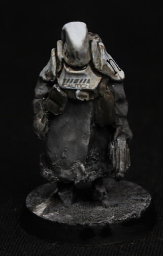 A painted mini of a human in dark grey coat. They wear dirty-white heavy armour on the upper body. There are caution signs on it.