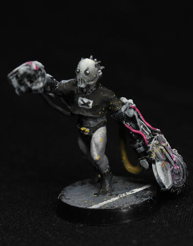 A running figure of a cyborg with giant metal hands, one of which is a circular saw. They wear a black T-shirt and a mask.