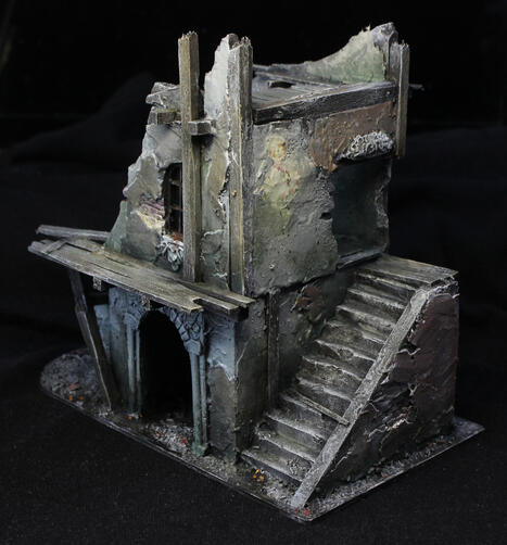 An old-fashioned ruined house with a complex shape. A staircase goes up to the second floor above an archway.